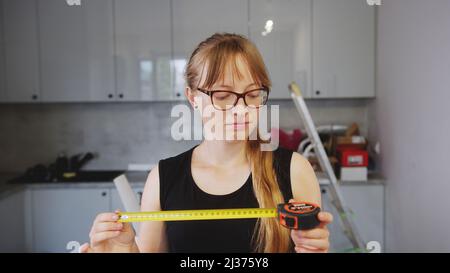 Rookie blue collar worker woman looking at a tape measure. Young female creator using a tape measure. Indoor shot. High quality photo Stock Photo