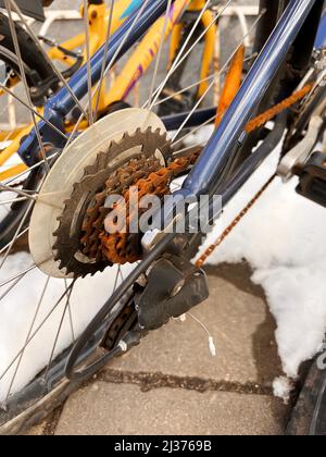 Blue bike has been outside all winter and got broken. Rusty bicycle chain hangs on sprocket and gear. Stock Photo