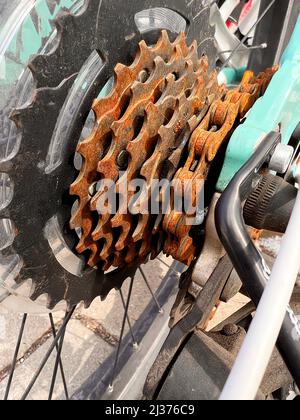 Blue bike has been outside all winter and got broken. Rusty bicycle chain hangs on sprocket and gear. Stock Photo