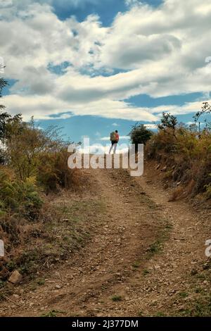 man with backpack on top of uphill dirt road against dramatic sky in the Nebrodi Park, Sicily Stock Photo