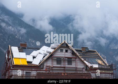 Photo of the renovation of the roof of an old house with erected scaffolding and new roofing and insulation as a concept for renovation of aged buildi Stock Photo