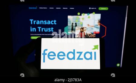 Person holding smartphone with logo of Portuguese risk management company Feedzai on screen in front of website. Focus on phone display. Stock Photo