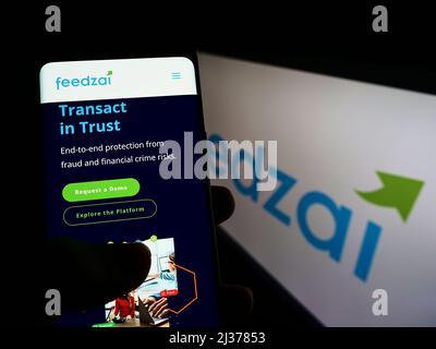 Person holding smartphone with website of Portuguese risk management company Feedzai on screen in front of logo. Focus on center of phone display. Stock Photo