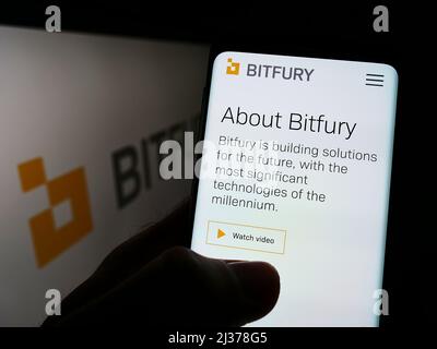 Person holding cellphone with webpage of Dutch blockchain company Bitfury Holding B.V. on screen with logo. Focus on center of phone display. Stock Photo