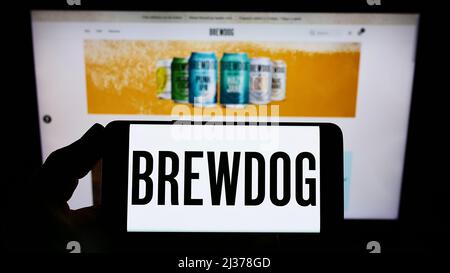 Person holding smartphone with logo of British brewery company BrewDog plc on screen in front of website. Focus on phone display.
