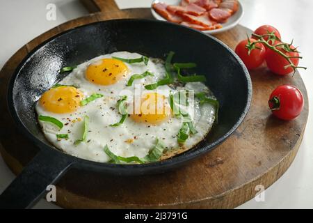Fried Eggs In A Frying Pan, Bacon and Cherry Tomatoes Stock Photo