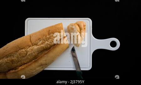 Cut bread into slices, bread slices on chopping board with knife, isolated on black background, top view Stock Photo