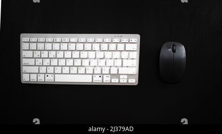 White wireless keyboard and black mouse on desk, isolated on black background, top view Stock Photo