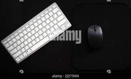 White wireless keyboard and black mouse on desk, isolated on black background, top view Stock Photo