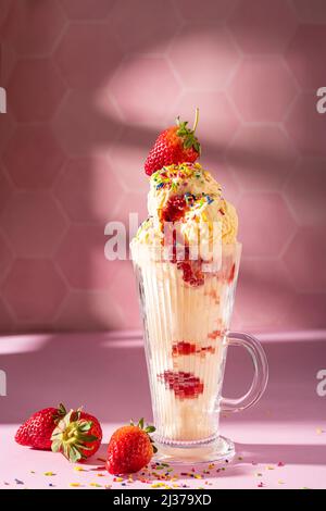 Vanilla ice cream milkshake garnished with fresh strawberry and colourful sprinkles on pink background Stock Photo