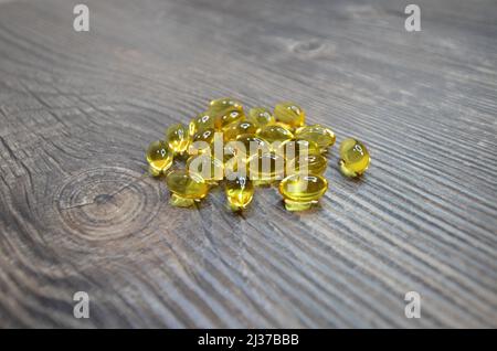 The oil fish laying on the wooden table. Yellow oil fish capsules close up photo. Stock Photo