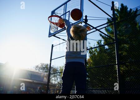 A little blond boy throwing a basketball on a cloudless sunny day Stock Photo