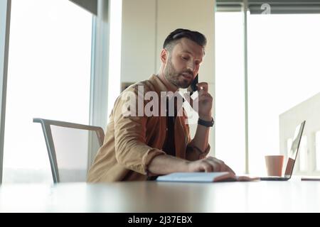Businessman Talking On Phone Taking Notes Working Sitting At Workplace Stock Photo