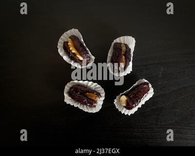 Top down view of dried dates in paper cups and stuffed with various nuts placed on a black wooden table. Stock Photo