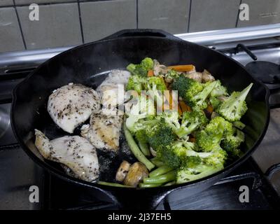 A mix of vegetables and chicken mixed with herbs, pepper and salt being cooked on a cast iron skillet. Stock Photo