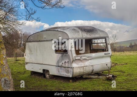 02.04.2022 Kirkby Stepheny, Cumbria, UK. White vintage caravan with all its windows broke sitting deralict in a field Stock Photo