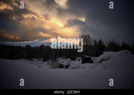 storm clouds in the sky at the sunset on Mount Etna National Park covered in snow, Sicily, Italy Stock Photo