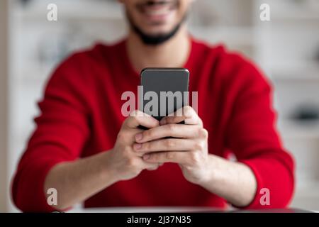 Closeup Shot Of Bearded Arab Guy Sitting At Desk And Using Smartphone Stock Photo