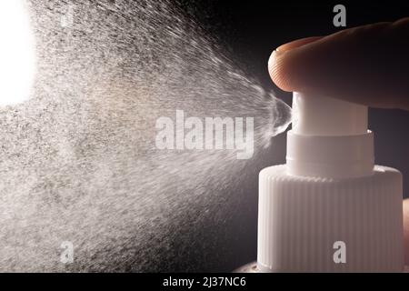 Liquid sprayed from a spray bottle towards a light source. A finger is pressing on the bottle. The droplets spread rapidly linearly. Stock Photo