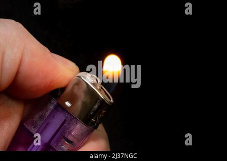 Lighting a lighter close-up. Transparent purple plastic gas chamber lighter lit by a hand. Stock Photo