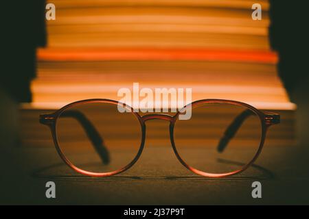 Close-up glasses in selective focus. There are books stacked on top of each other out of focus. Education, reading, eye health, rest, leisure concept. Stock Photo