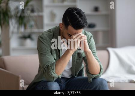 Portrait Of Depressed Middle Eastern Guy Sitting On Couch At Home Stock Photo