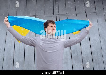 A man holds the state flag of Ukraine outdoors in snowy spring weather. Ukrainian flag, patriotism. Defender of the country, his land and family. Ukra Stock Photo
