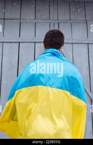 The man is wearing the state flag of Ukraine on his shoulder and is standing with his back to the camera outdoors in snowy weather. Ukrainian flag, pa Stock Photo