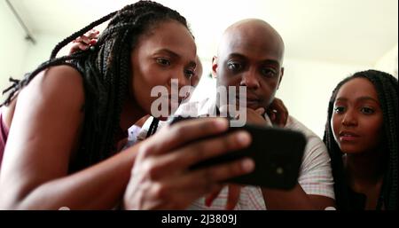 African family shock reaction looking at cellphone device. parents and children surprise reaction to smartphone news Stock Photo