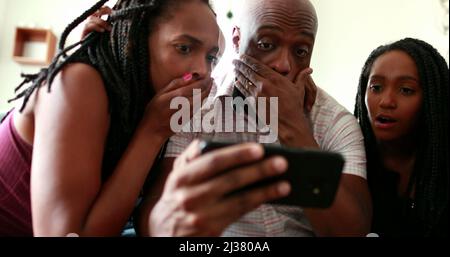 African family shock reaction looking at cellphone device. parents and children surprise reaction to smartphone news Stock Photo