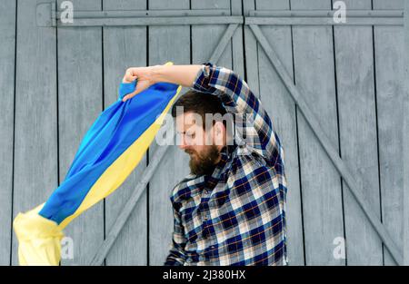 A man in a shirt holds the national flag of Ukraine outdoors in snowy spring weather. Ukrainian flag, patriotism. Defender of the country, his land an Stock Photo