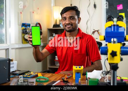 happy repairman showing green screen mobile phone by looking camera at shop - concept of online repair booking service, app promotion and Stock Photo