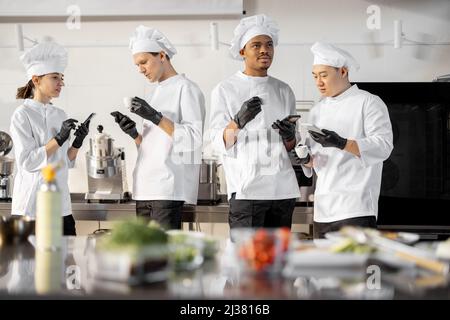 Team of multiracial cooks having conversation during a coffee break in the kitchen. Well-dressed chefs resting and having fun in the restaurant kitchen. Teamwork and leisure time on work Stock Photo