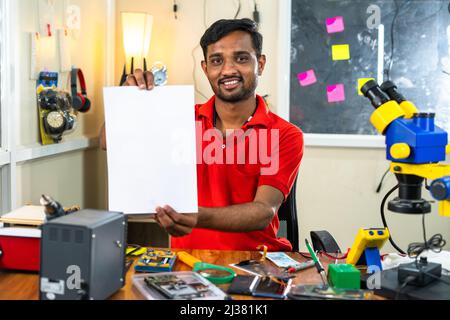 Smiling technician showing completion certificate by looking camera at workshop - concept of advertisement, professional occupation and mobile repair Stock Photo