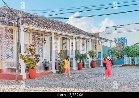 Two girls tourists taking pictures on street near restaurant in colonial old town. Trinidad, Cuba. Stock Photo