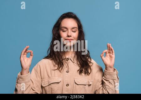 Serene happy pretty young european woman with closed eyes meditates, enjoys silence and relaxation Stock Photo