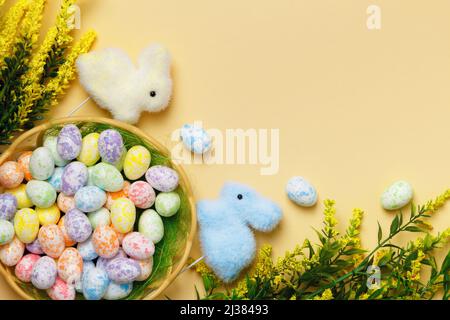 Easter eggs in a basket of toy rabbits flowering branches on a yellow background with a place for text. Stock Photo
