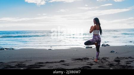 woman in sport clothes practicing yoga and meditating on beach in morning Stock Photo