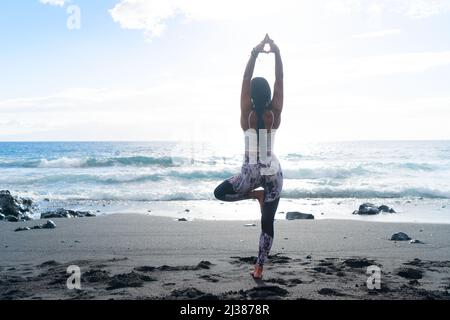 woman in sport clothes practicing yoga and meditating on beach in morning Stock Photo