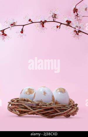 Branch of cherry, apricot, sakura with eggs painted white and gold in nest. Happy Easter. Vertical. Copy space Stock Photo