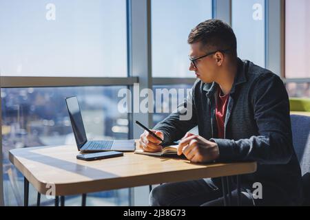 Successful manager working with cafe business information, investment report, writing notes while doing online research on laptop computers, digital m Stock Photo