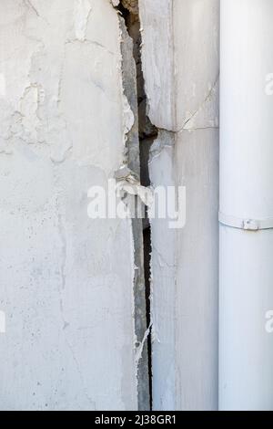 A large crack in the white concrete wall of the urban house, can see the brick block as the main structure caused by soil subsidence, front view with Stock Photo