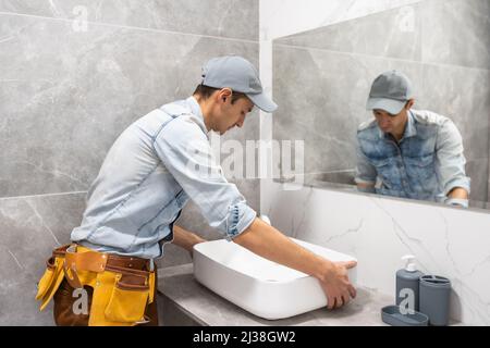 Professional plumber, male worker in uniform installing sink and water pipe in new apartment Stock Photo