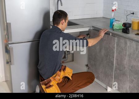 Smiling handyman, kitchen carpenter worker in overalls smiling at camera while installing kitchen furniture Stock Photo