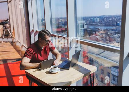 Smart software developer sitting at desktop in coworking space with laptop and creating publishing idea, using netbook for messaging and networking du Stock Photo