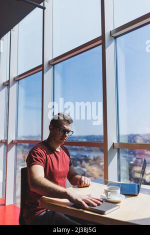 Smart software developer sitting at desktop in coworking space with laptop and creating publishing idea, using netbook for messaging and networking du Stock Photo