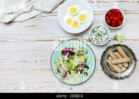 Breakfast table with fresh salad, hard boiled eggs, cottage, sausages and tomatoes. Copy space, wooden background. Stock Photo