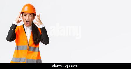 Mad and outraged asian female chief engineer, construction manager burst in rage, losing temper at employees, shouting and shaking hands aggressive Stock Photo