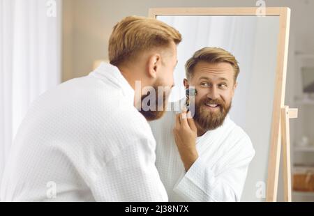 Happy man looking in mirror and massaging his face with jade facial beauty roller Stock Photo