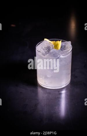 A vertical close-up of gin and tonic with lime and ice cubes in a glass on a bar table with lighting Stock Photo